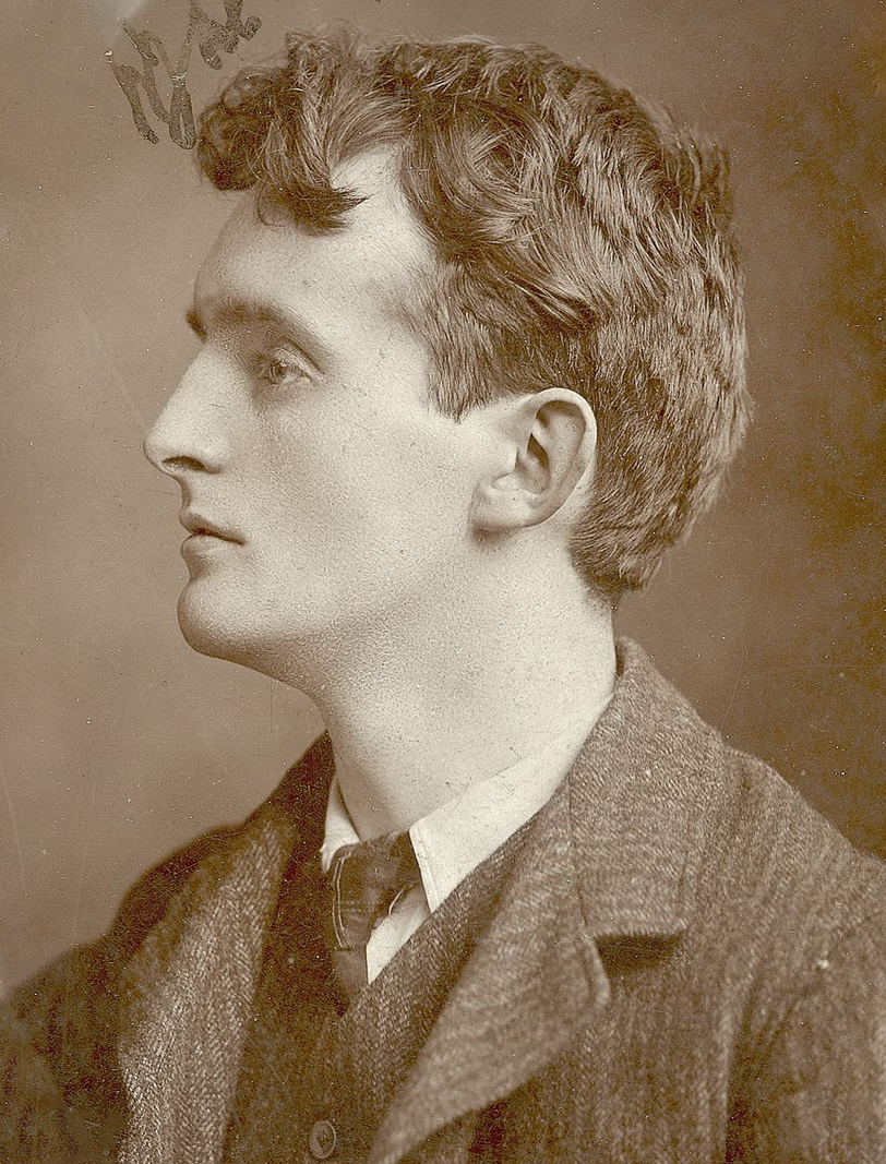 A black and white profile headshot image of Padraic Colum who appears to be wearing a waist jacket and tie under a wool coat.